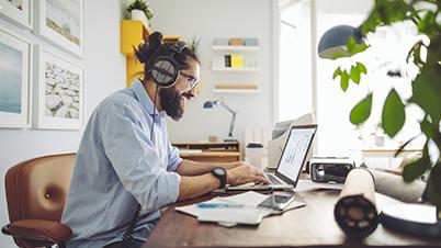 一个男人戴着耳机，坐在办公桌前，手里拿着一台笔记本电脑